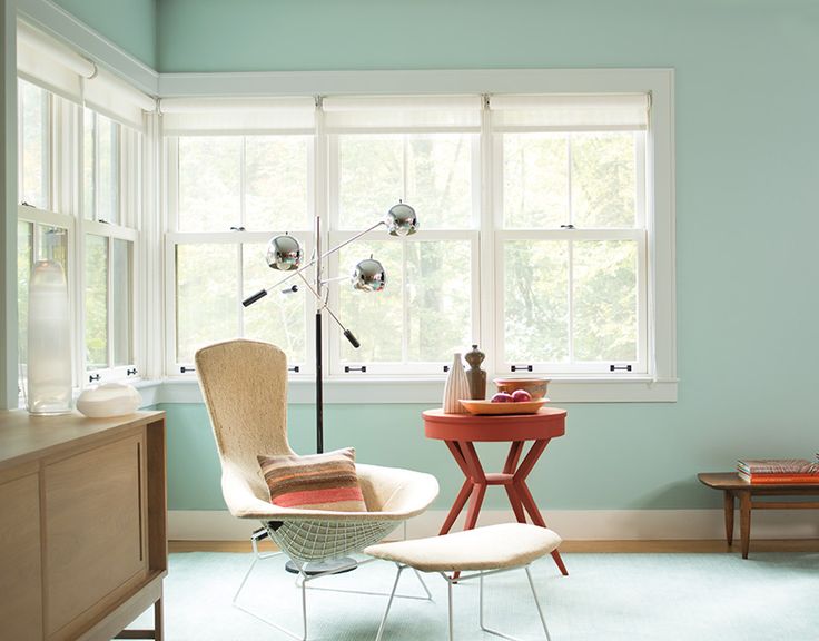 a living room with blue walls and white trimmings, including a chair in front of a window