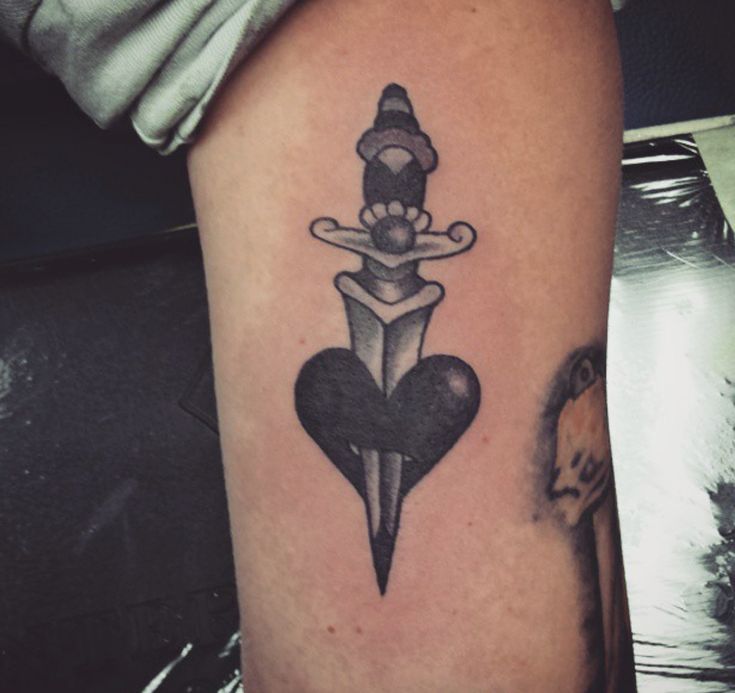 a tattoo on the arm of a person with a dagger and heart in front of it