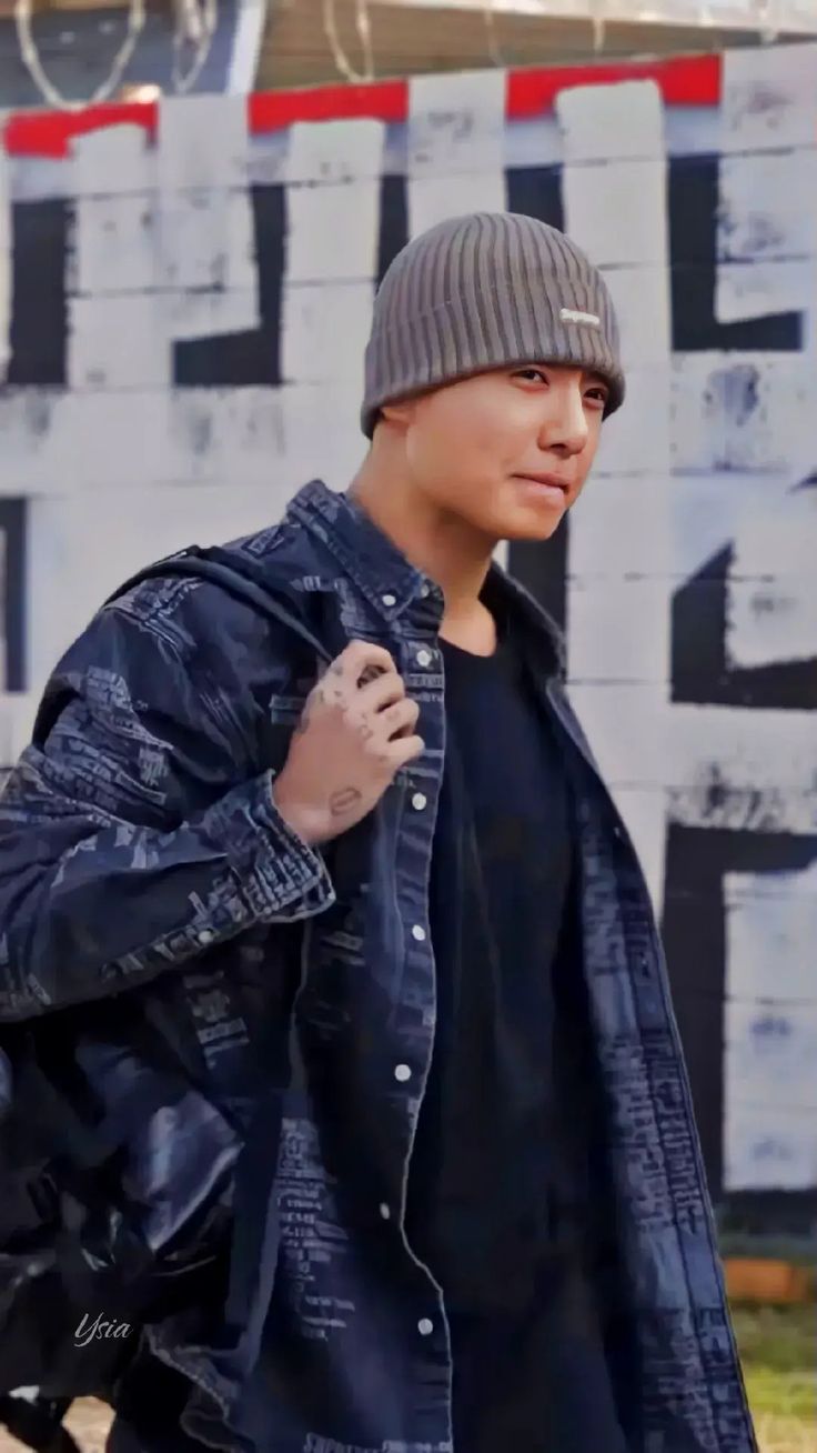 a young man wearing a beanie and jacket is standing in front of a graffiti wall