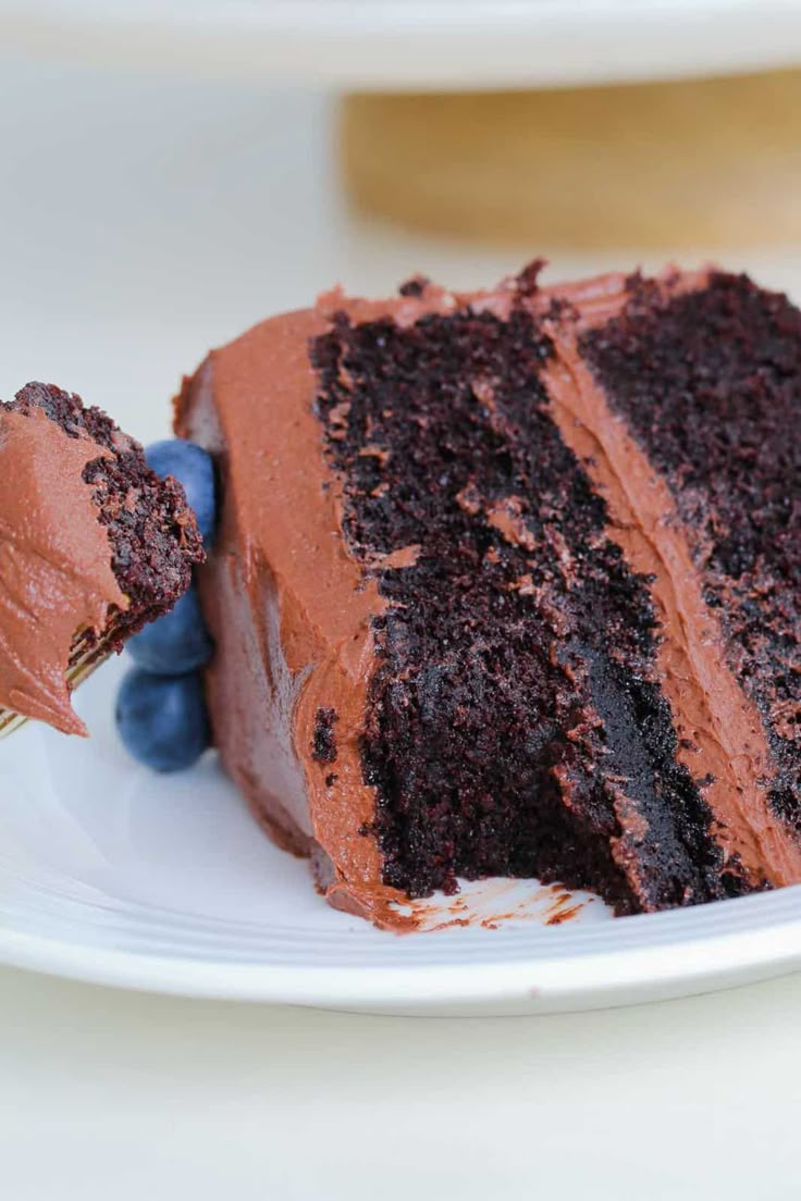 a piece of chocolate cake on a white plate with blueberries and a fork in it