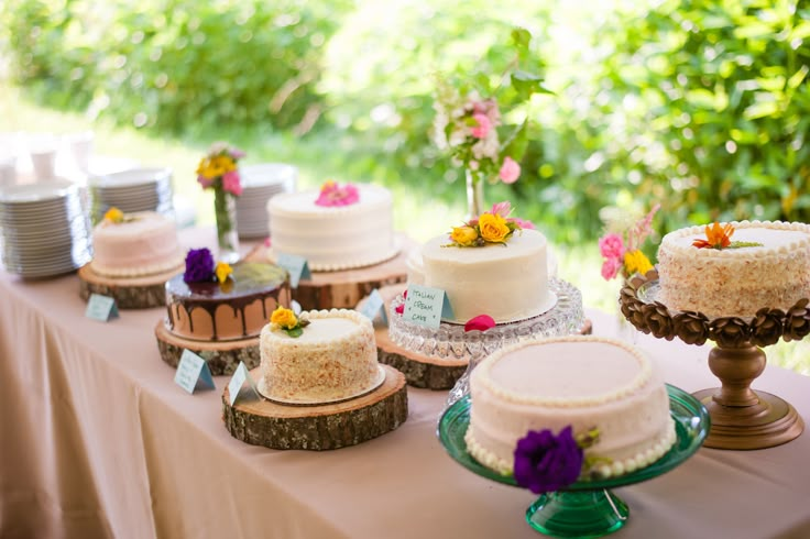 a table topped with lots of cakes and desserts on top of wooden slices covered in frosting