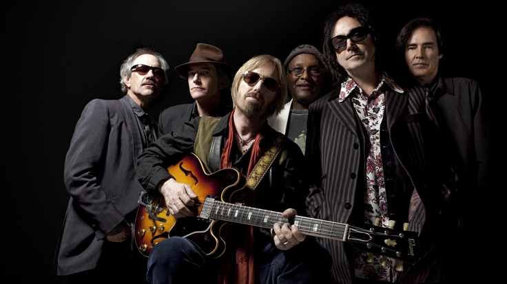 a group of men standing next to each other with guitars in their hands and one man holding an electric guitar