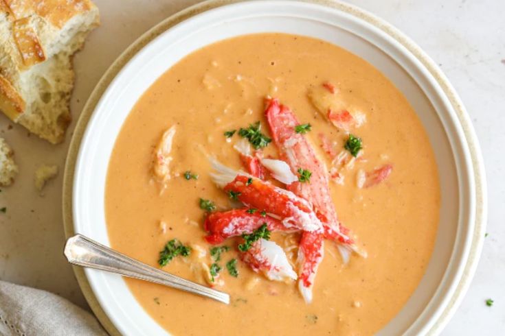 a bowl of soup with lobster and bread on the side