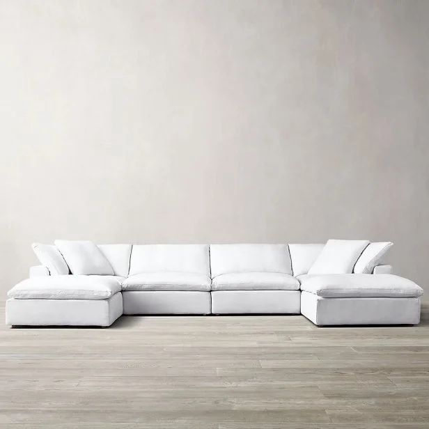 a large white sectional couch with pillows on the top and bottom, in front of a gray wall