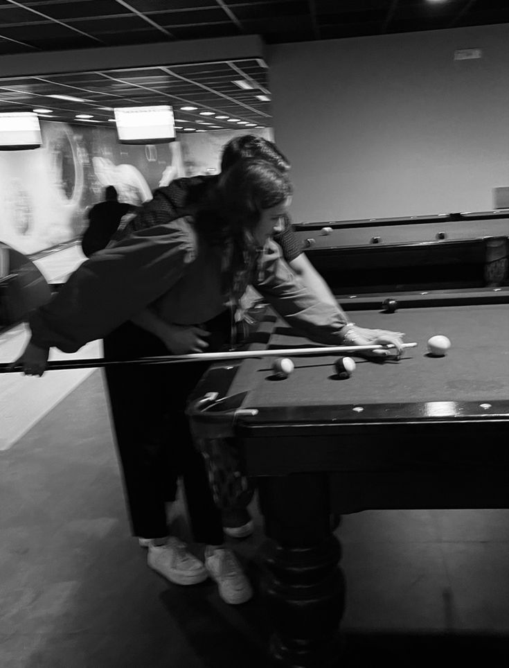 two people are playing pool in a large room with black and white photos on the walls