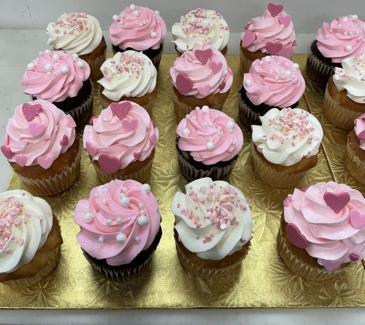 cupcakes with pink and white frosting are arranged on a gold tray