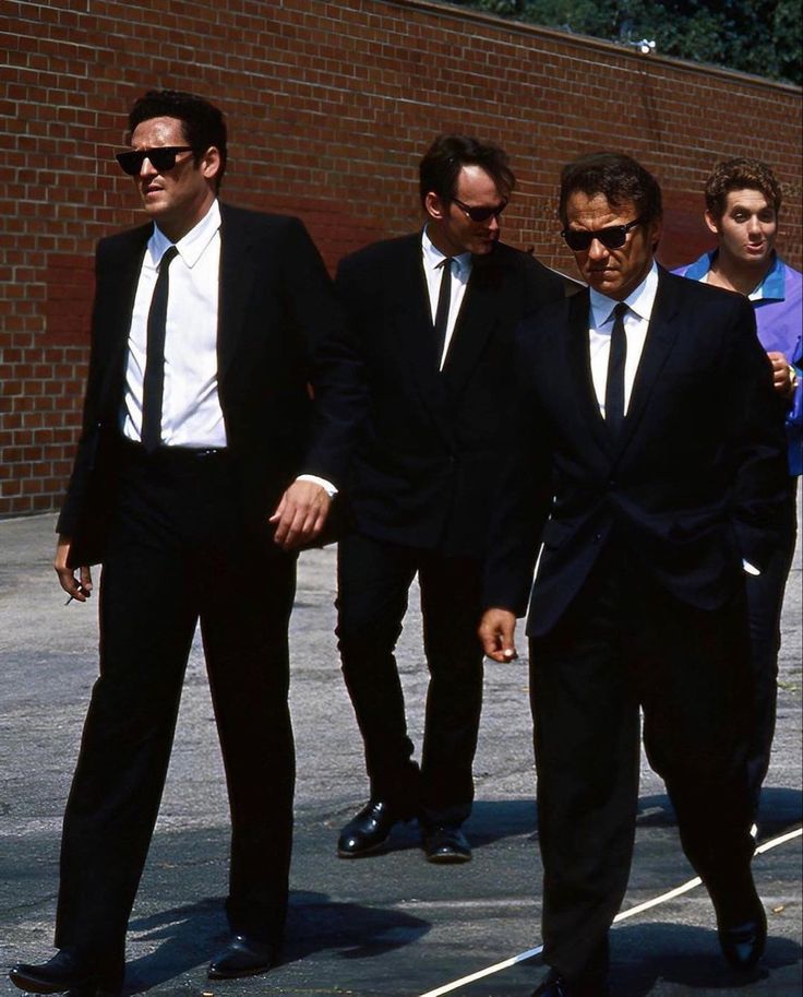 three men in suits and sunglasses walking down the street