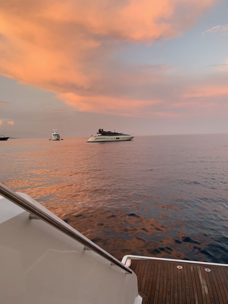 two boats are sailing in the ocean under a pink sky with clouds above them and one boat is out on the water