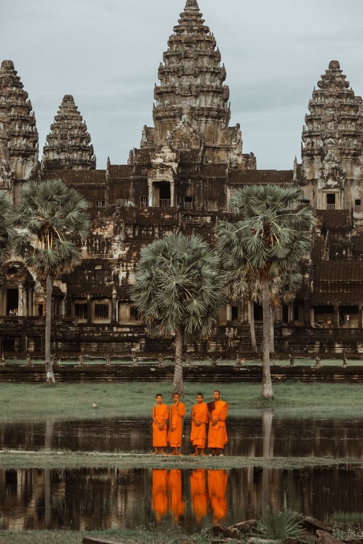 three monks in orange robes are standing next to some palm trees and the water is reflecting them