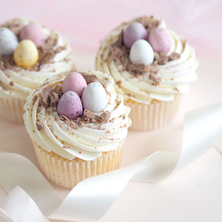 three cupcakes with white frosting and chocolate eggs