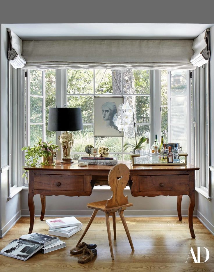 a wooden desk sitting next to a window with pictures on the wall and a lamp