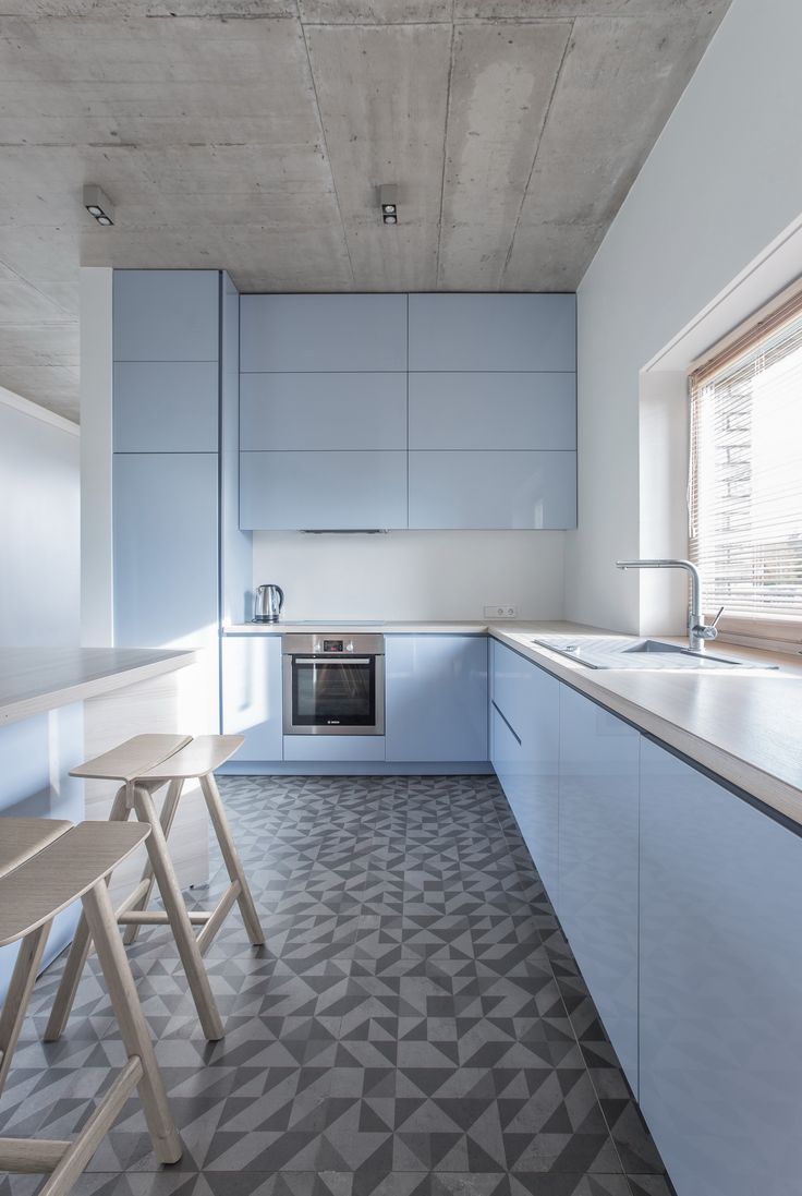 an empty kitchen with blue cabinets and white counter tops, two stools in the foreground