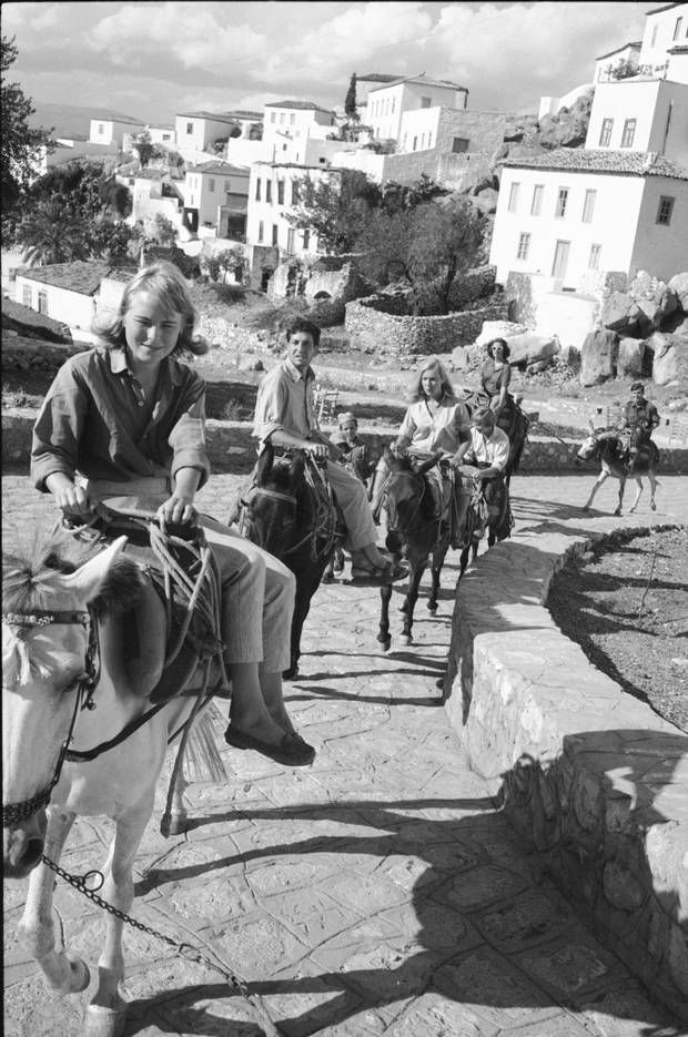 black and white photograph of people riding donkeys on the street with buildings in the background