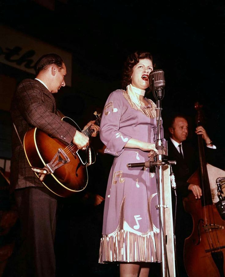 a woman singing into a microphone next to a man holding a guitar and an instrument