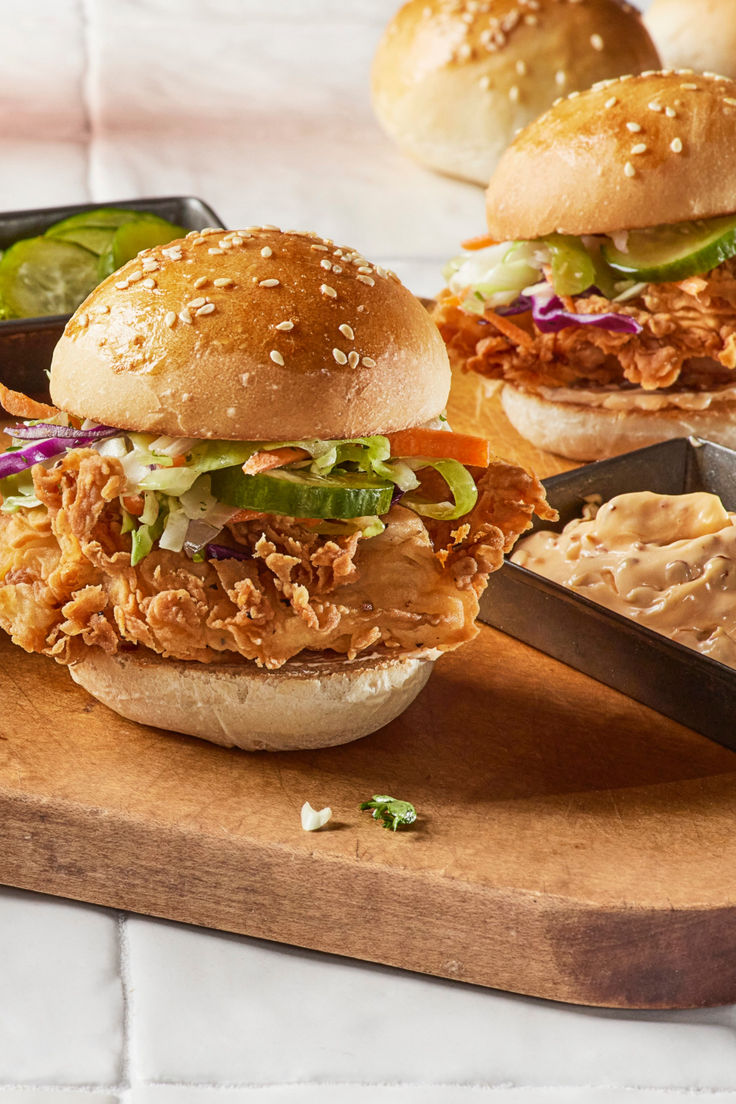 two pulled pork sandwiches with coleslaw and pickles on a cutting board next to dipping sauces