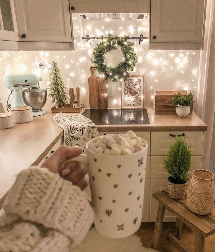 a person holding a cup filled with marshmallows in front of a kitchen counter