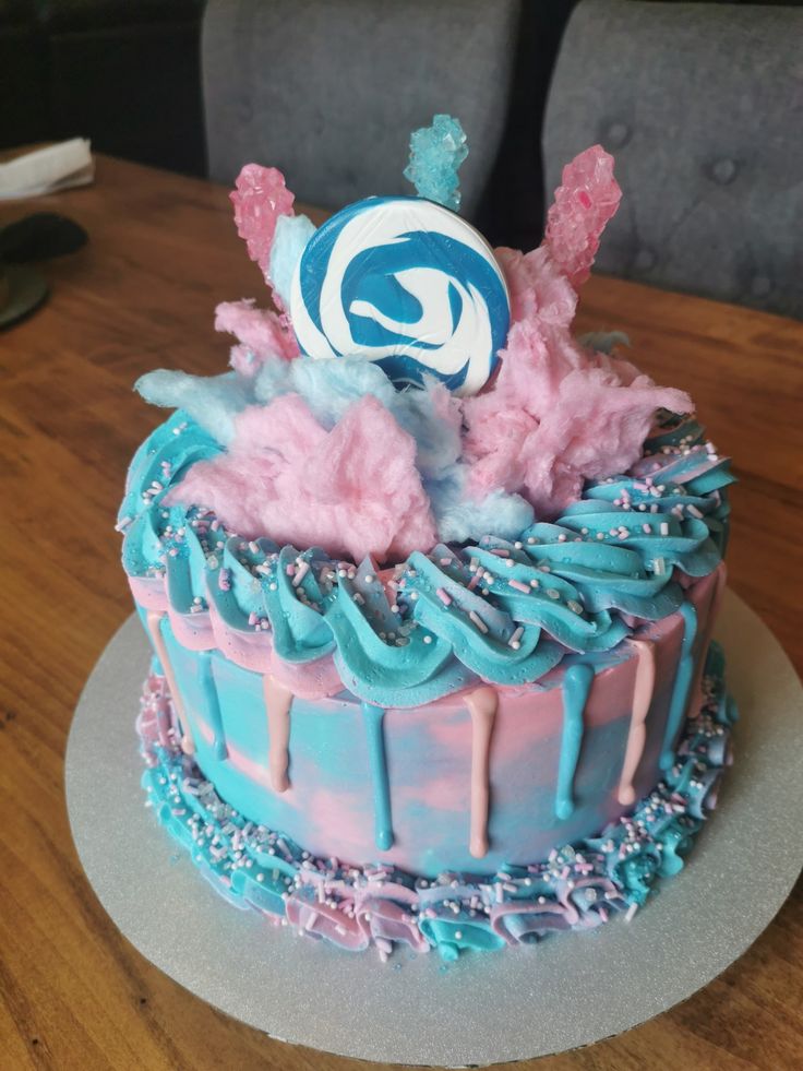 a blue and pink cake sitting on top of a wooden table covered in frosting