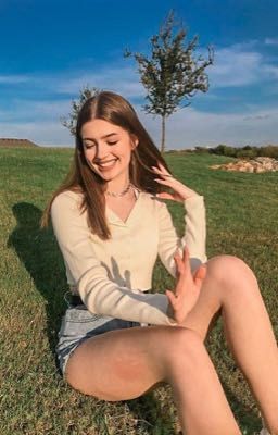 a woman sitting in the grass with her hand on her head and smiling at the camera