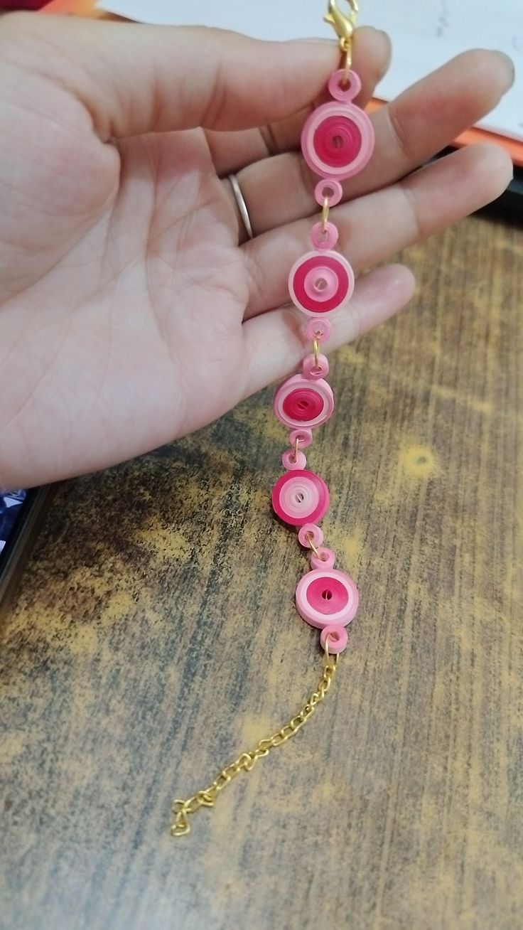 a person is holding a pink and gold chain with buttons attached to it on a wooden table