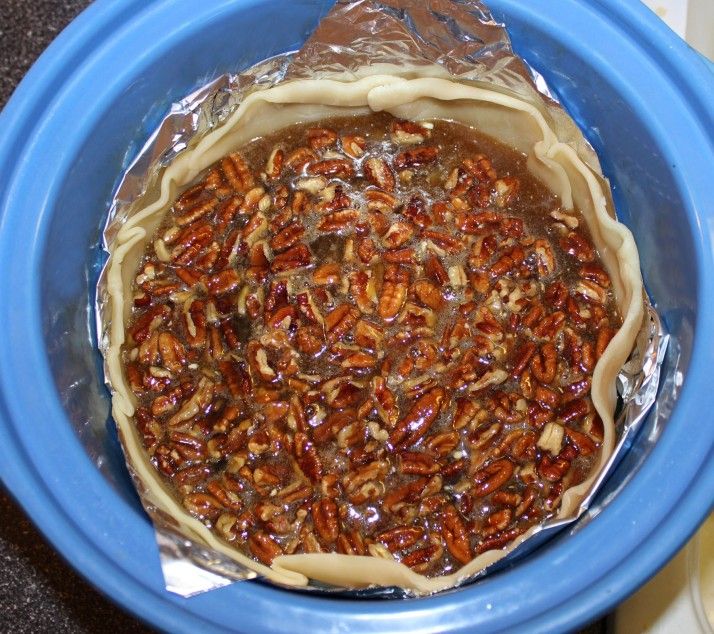 a pie in a blue bowl with pecans on top and tin foil covering it