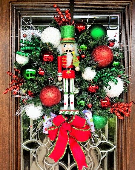 a christmas wreath with nutcrackers, ornaments and decorations hanging on the front door