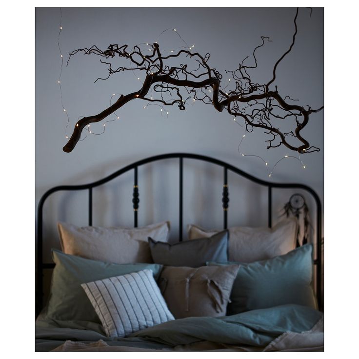 a bed with pillows and lights hanging from the headboard, in front of a tree branch