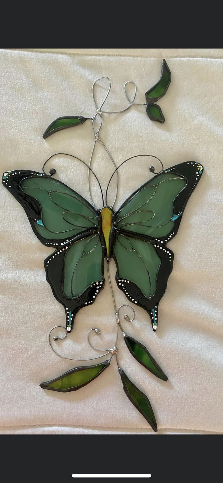 a green and black butterfly sitting on top of a white bed sheet with leaves attached to it