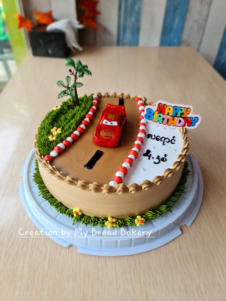 a birthday cake decorated with a race track and car on it's side, sitting on a table