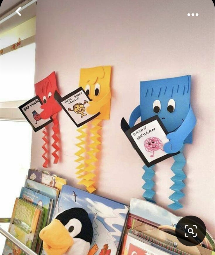 there are some books on the wall with pictures hanging from them and one penguin is holding a book in his hand