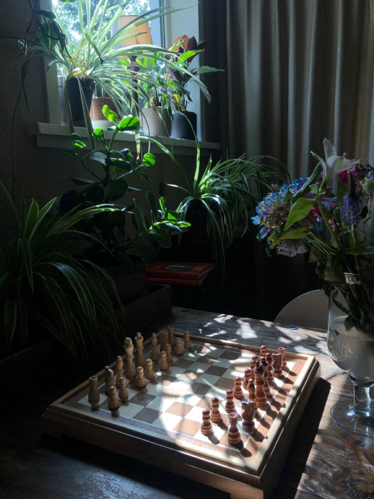 a wooden chess board sitting on top of a table next to a potted plant