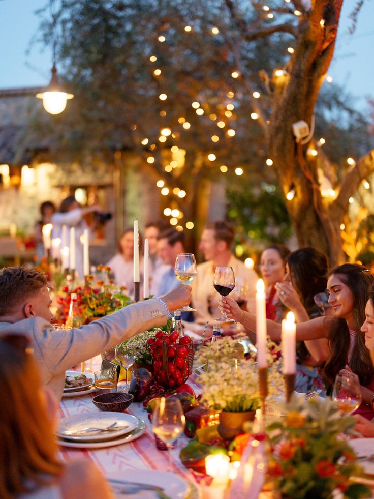 a group of people sitting around a dinner table with wine glasses in their hands and candles lit