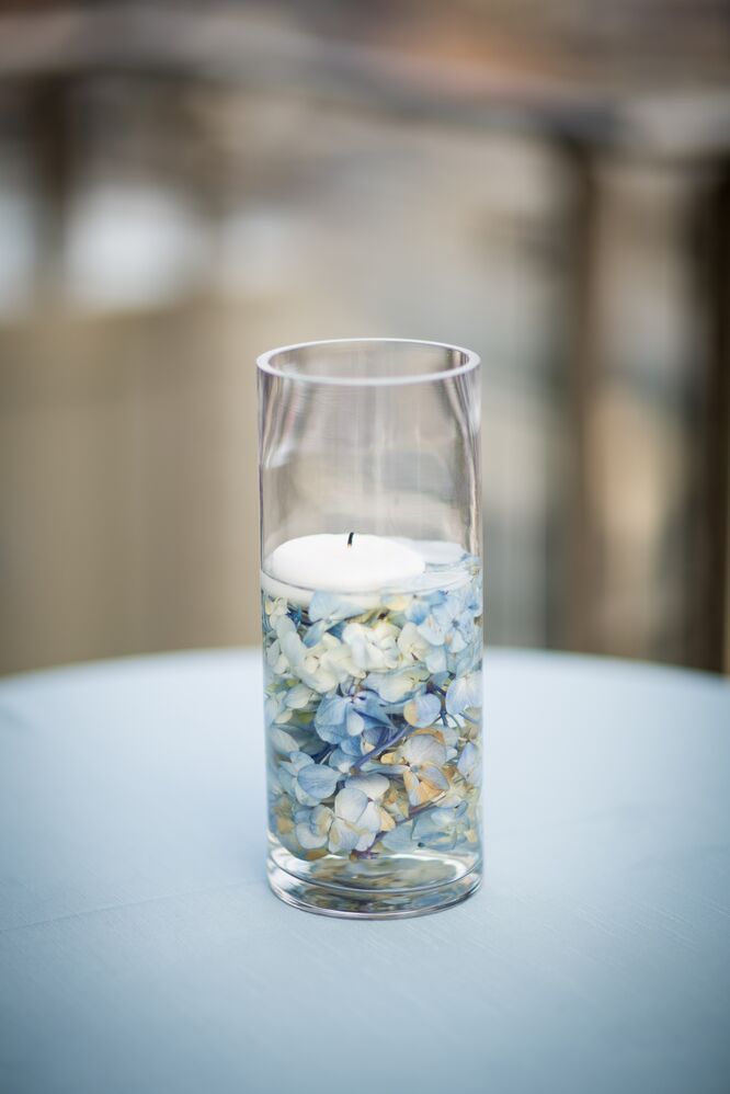 a glass vase filled with water and a lit candle on top of a white table