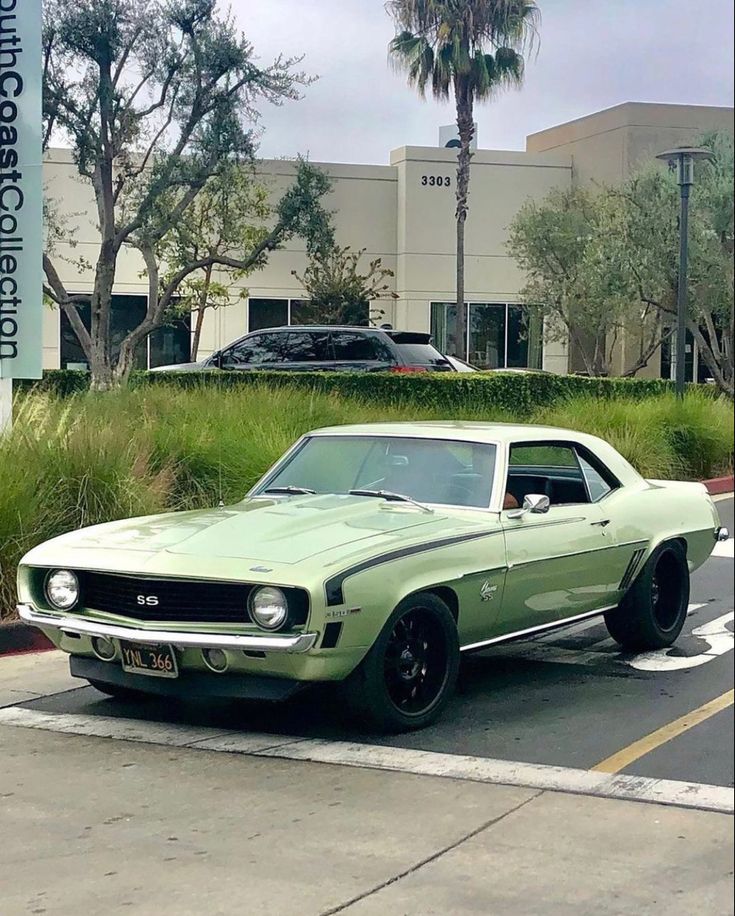 a green muscle car parked in a parking lot next to a building and palm trees