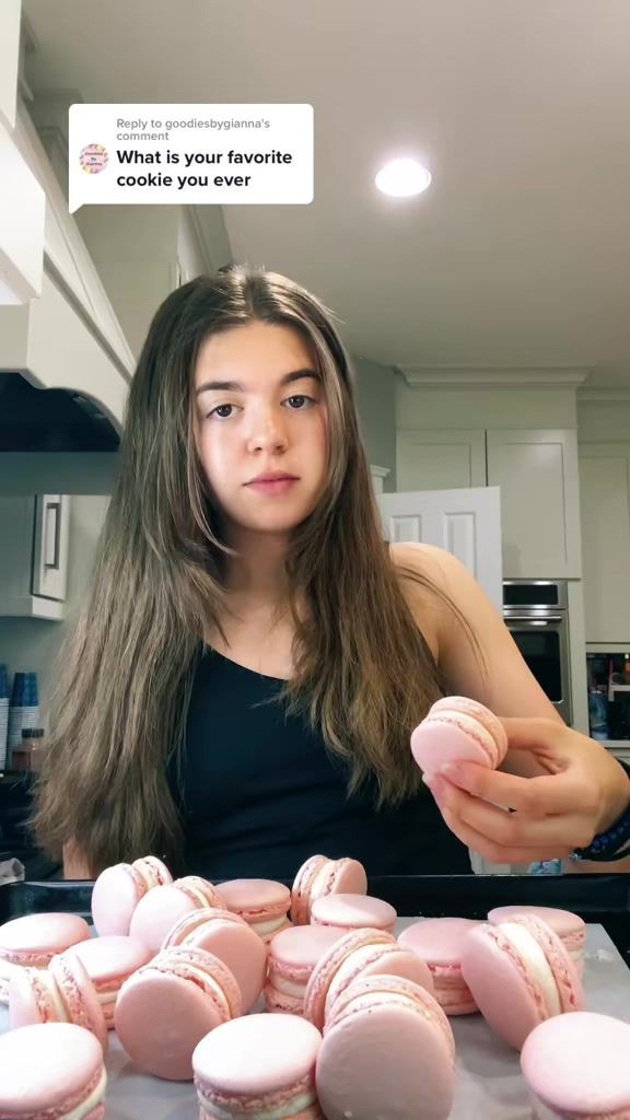 a woman is holding up some pink macaroons