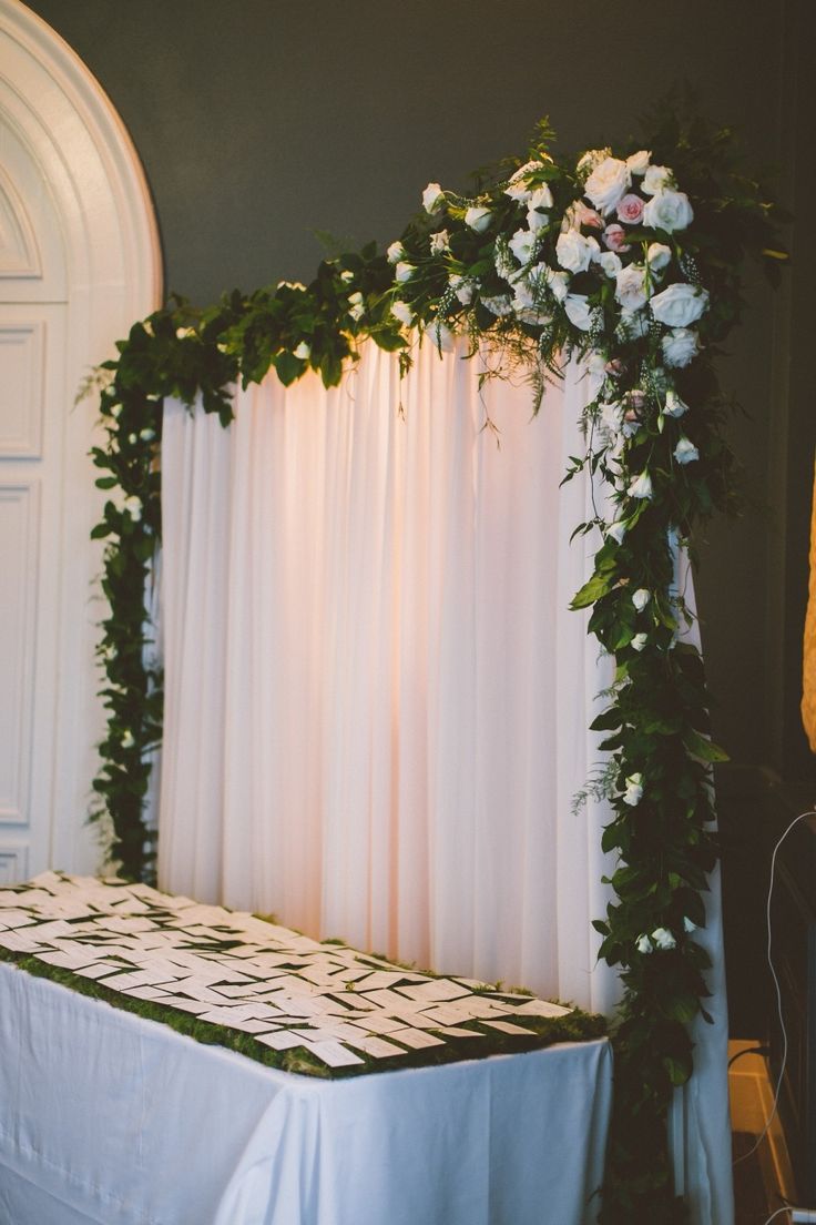 an arch with flowers and greenery on it is next to a white curtain in front of a door