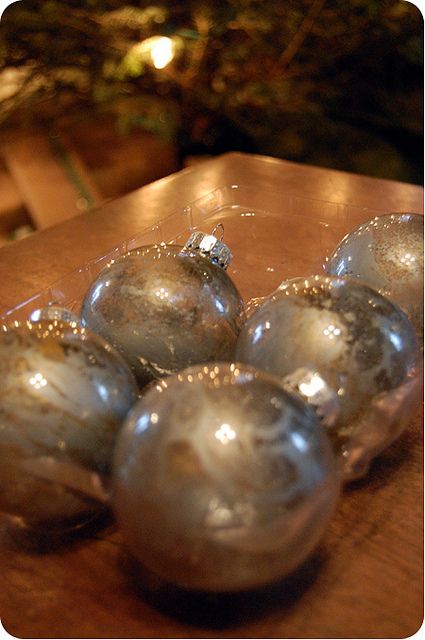 silver ornaments are sitting on a wooden table in front of a christmas tree and lights