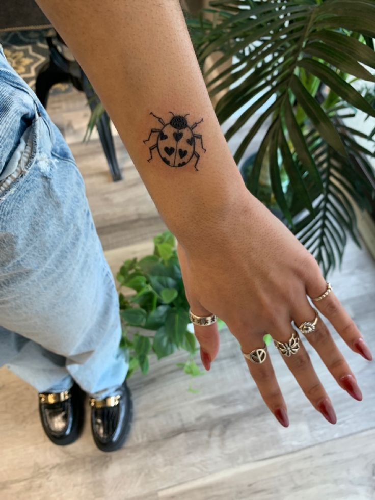 a ladybug tattoo on the left wrist and right hand is shown in front of a potted plant