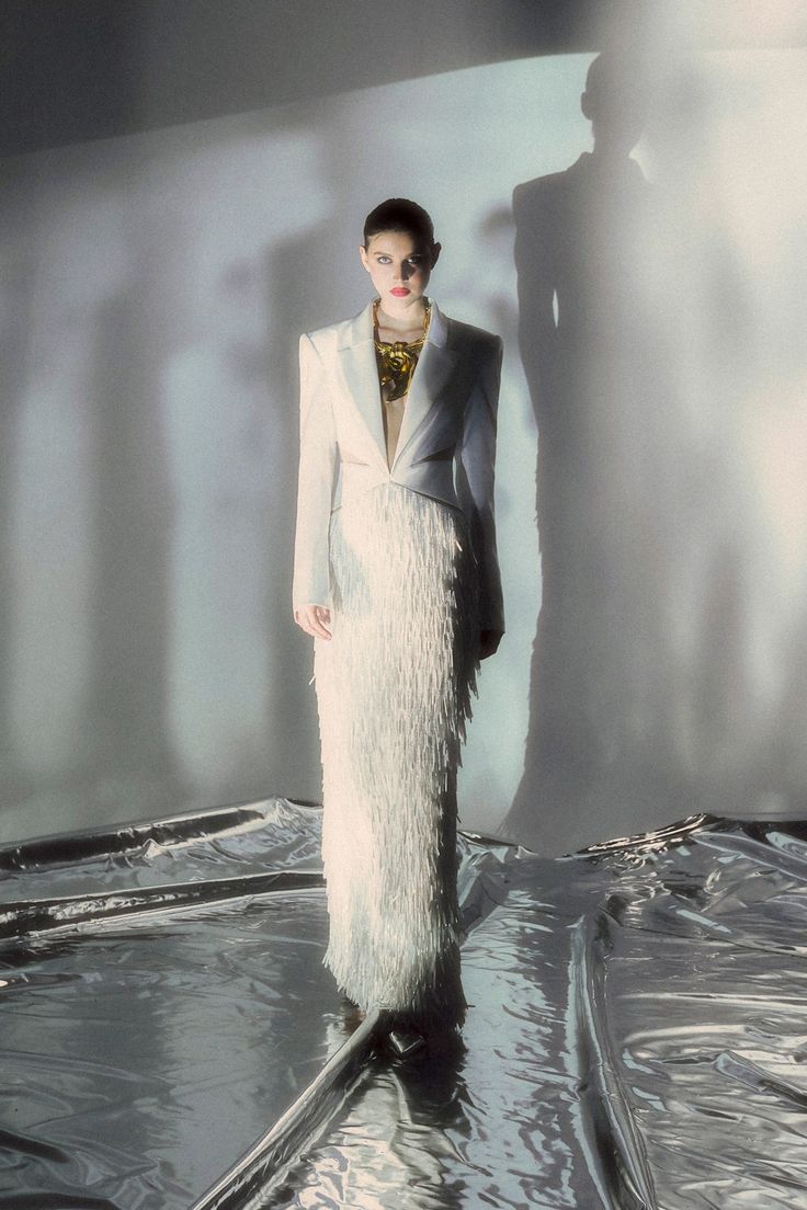 a woman in a long white dress and jacket standing on a surface with water flowing around her