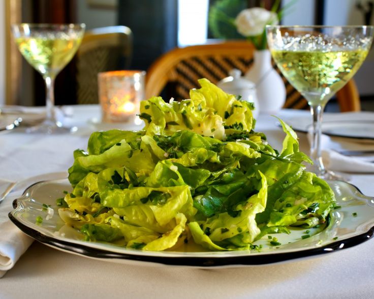 a white plate topped with lettuce next to two wine glasses