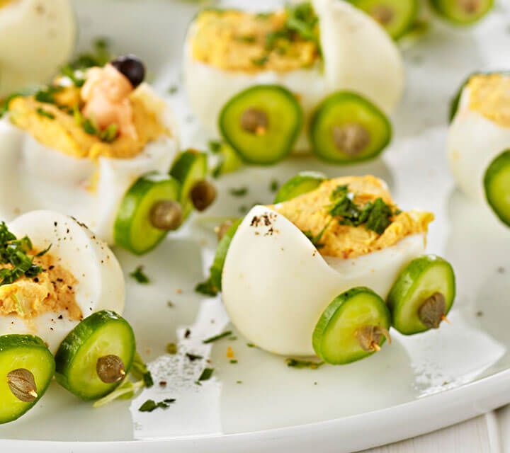 deviled eggs with cucumbers and other toppings on a white platter