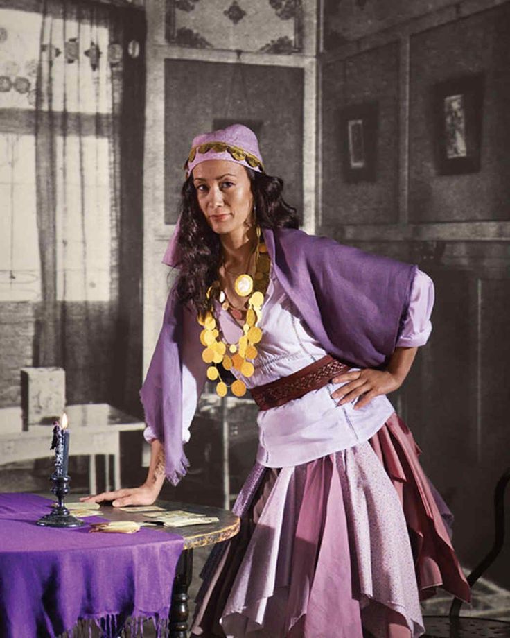 a woman dressed in costume standing next to a table with a purple cloth on it