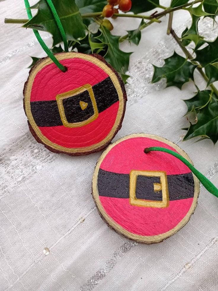 two wooden ornaments with santa claus's belt on them sitting next to holly branches