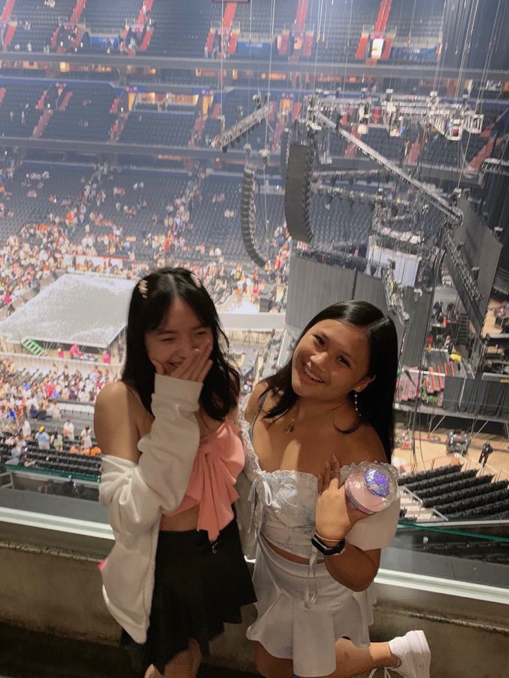 two young women standing next to each other in front of a large stadium filled with people