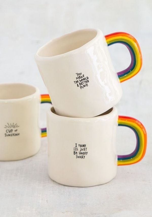 three white mugs with rainbow designs on them sitting in front of the same cup