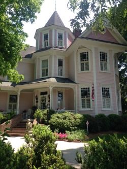 a large pink house sitting on top of a lush green forest next to tall trees