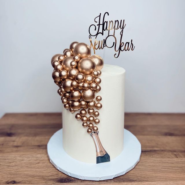 a white cake with gold decorations and a happy new year sign on top is sitting on a wooden table