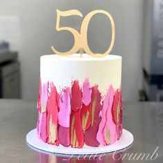 a white and pink cake with gold number 50 on top sitting on a wooden table