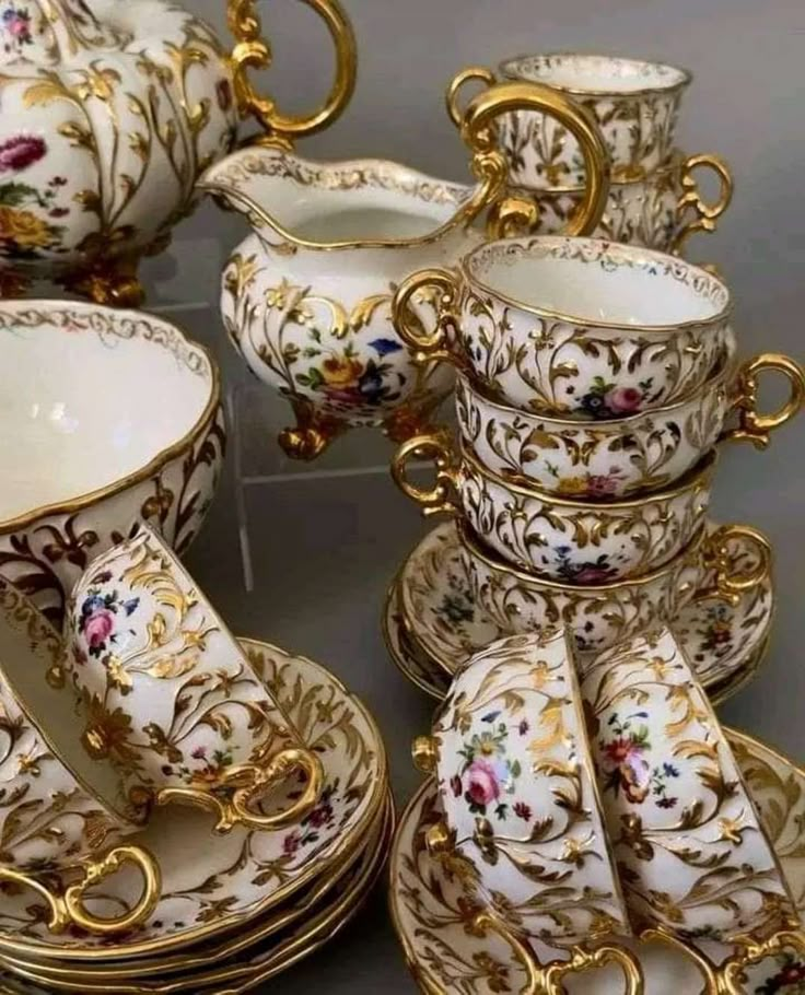 a table topped with lots of white and gold dishes covered in floral designs on top of each other