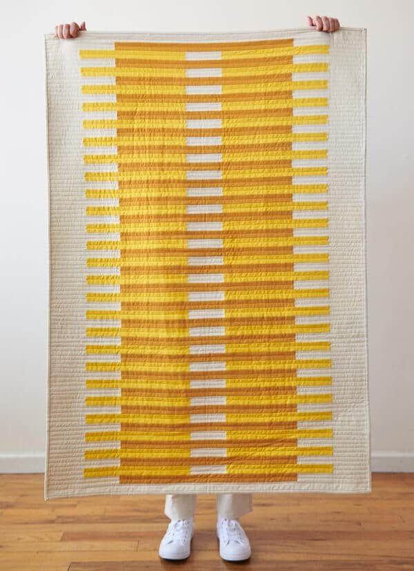 a person holding up a yellow and white quilt