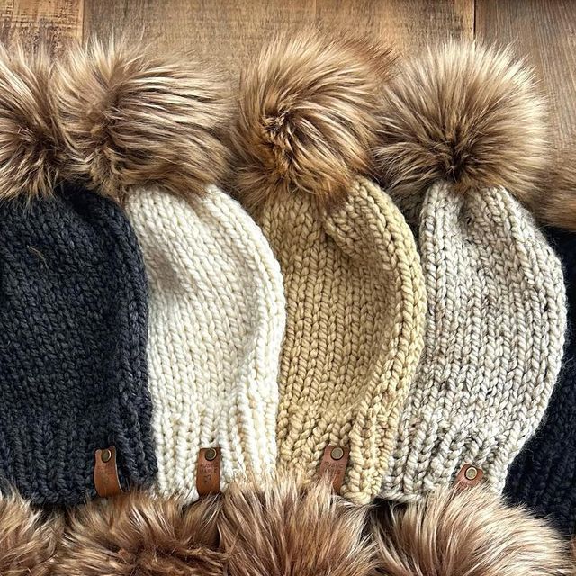 four hats with fur pom - poms lined up on top of each other